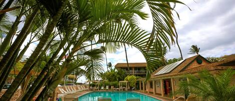 A pool area with lounge chairs, palm trees, and a building with a tiled roof.
