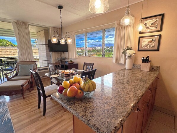A kitchen with a granite countertop, a dining area with chairs, a TV, and a view of the outdoors.