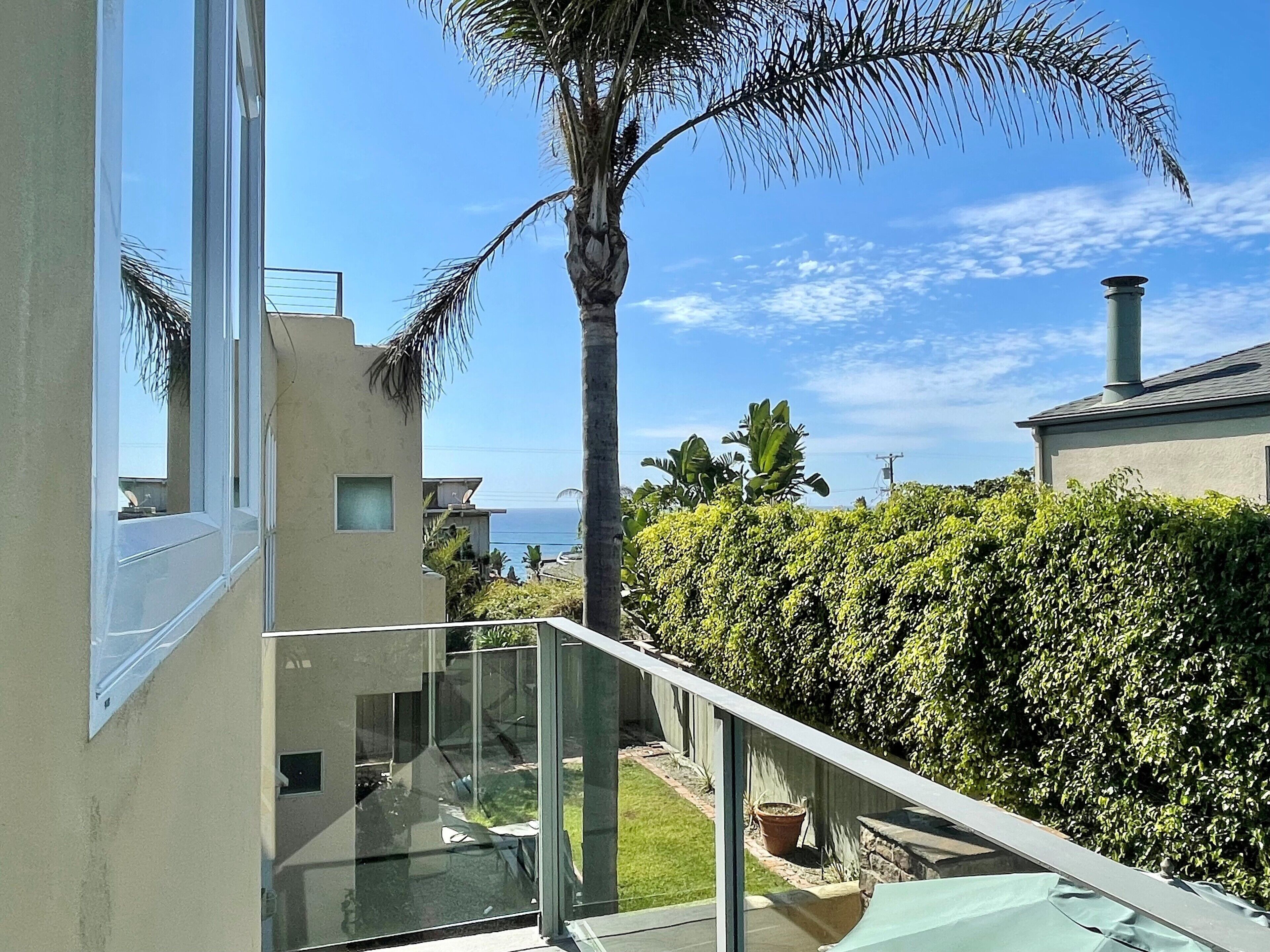 A modern residential building with a glass balcony overlooking a well-maintained garden and a clear view of the ocean.
