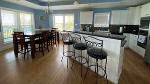 A modern kitchen with a central island, bar stools, wooden dining table, and white cabinets.