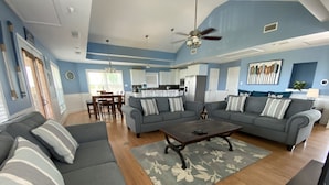 A spacious living room with a gray sectional sofa, a wooden coffee table, and a dining area with a table and chairs.