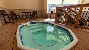 A hot tub on a wooden deck with a view of a town through a large window. -  LUXURY STUDIO+BUNK ROOM, VIEWS, MINS TO LIFTS /SHOPS, ONSITE HOT TUB, GARAGE (Copper Mountain)