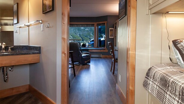 A hallway leading to a bedroom with a bed, a bathroom with a sink, and a dining area with chairs and a table. -  LUXURY STUDIO+BUNK ROOM, VIEWS, MINS TO LIFTS /SHOPS, ONSITE HOT TUB, GARAGE (Copper Mountain)