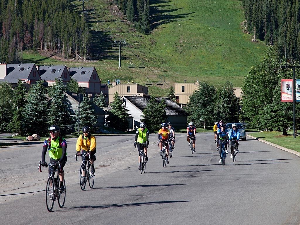 Eine Gruppe Radfahrer auf einer Straße, im Hintergrund Häuser und ein Hügel.