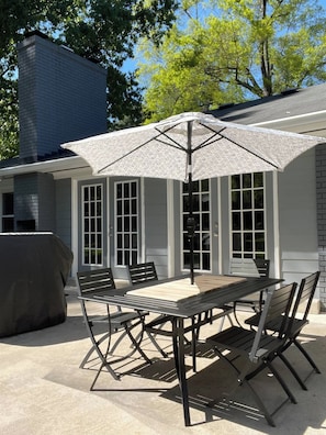 Eine Terrasse im Freien mit Tisch, Stühlen, Sonnenschirm und Grill.
