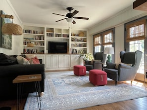 A living room with a ceiling fan, a television, bookshelves, a sofa, a chair, and a patterned rug.