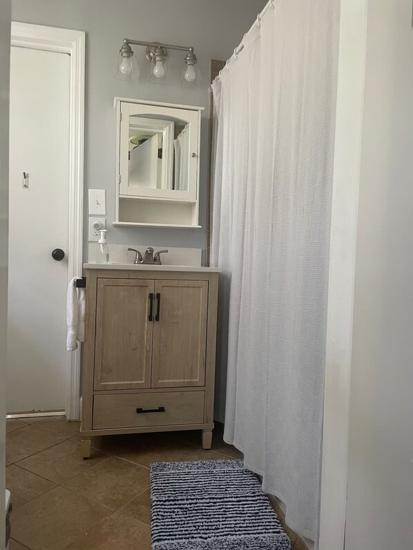 Un baño con un mueble de madera, un espejo, un lavabo y una cortina de ducha.