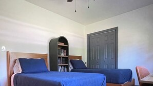 Una camera da letto con due letti in legno, una ventola a soffitto, una libreria e una porta.