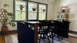 Zona pranzo con tavolo e sedie in legno, lampadario e libreria piena di libri.