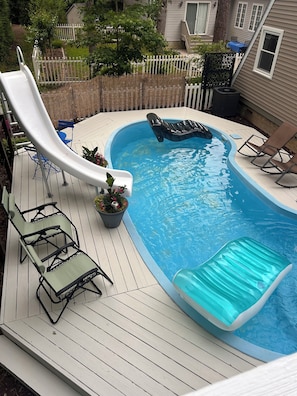 A swimming pool with a slide, lounge chairs, and a small inflatable float.