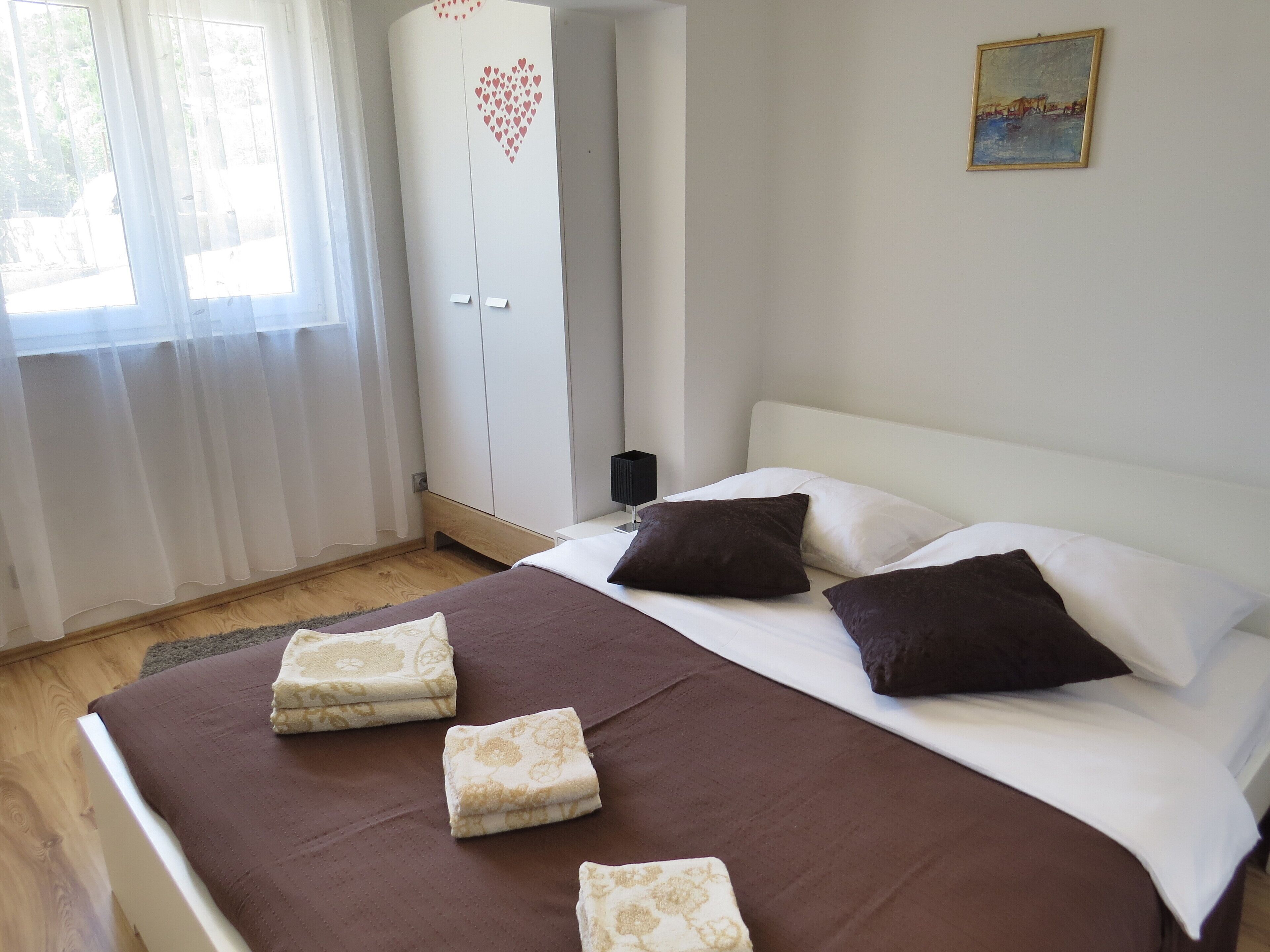 A bedroom with a bed, pillows, a nightstand, a wardrobe, and a painting on the wall.