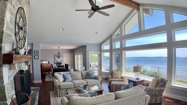 A spacious living room with a fireplace, large windows overlooking a body of water, and a cozy seating area. - Prime fall week Oct 10-17 available! Enjoy panoramic ocean views, near Camden (Northport)