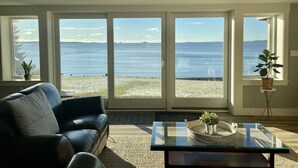 A living room with a sofa, a glass coffee table, and a view of the ocean through large sliding glass doors. - Prime fall week Oct 10-17 available! Enjoy panoramic ocean views, near Camden (Northport)