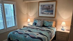 Ein Schlafzimmer mit einem Bett, zwei Nachttischen, einem Fenster mit Jalousien und einem Bild an der Wand.