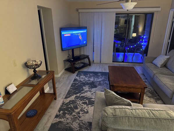 A living room with a television, sofa, coffee table, and a glass table with a decorative bowl.