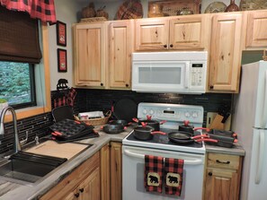 Una cocina con gabinetes de madera, un microondas blanco, una estufa y un lavamanos.