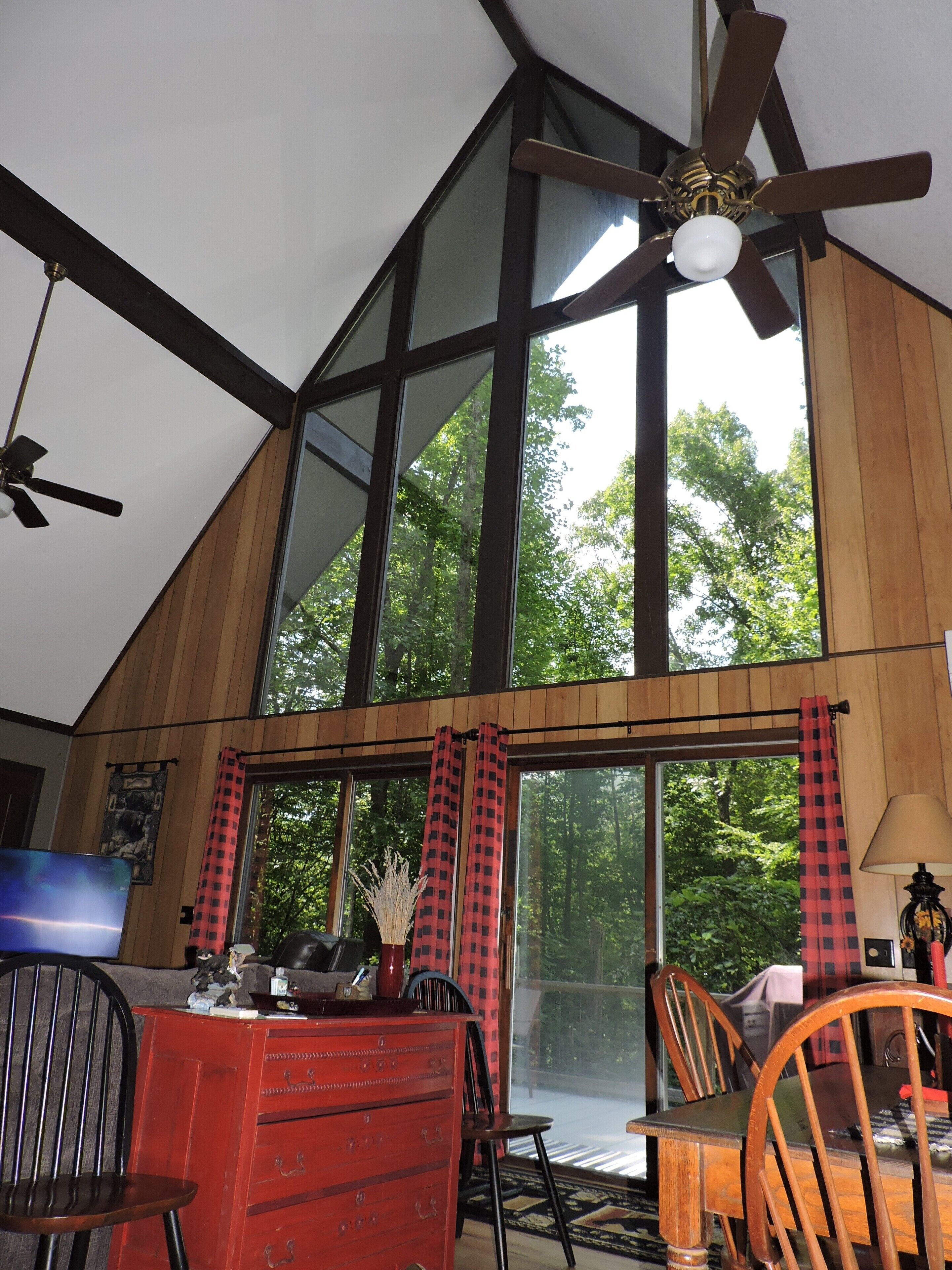 A room with a sloped ceiling, large windows, a ceiling fan, and a red dresser.