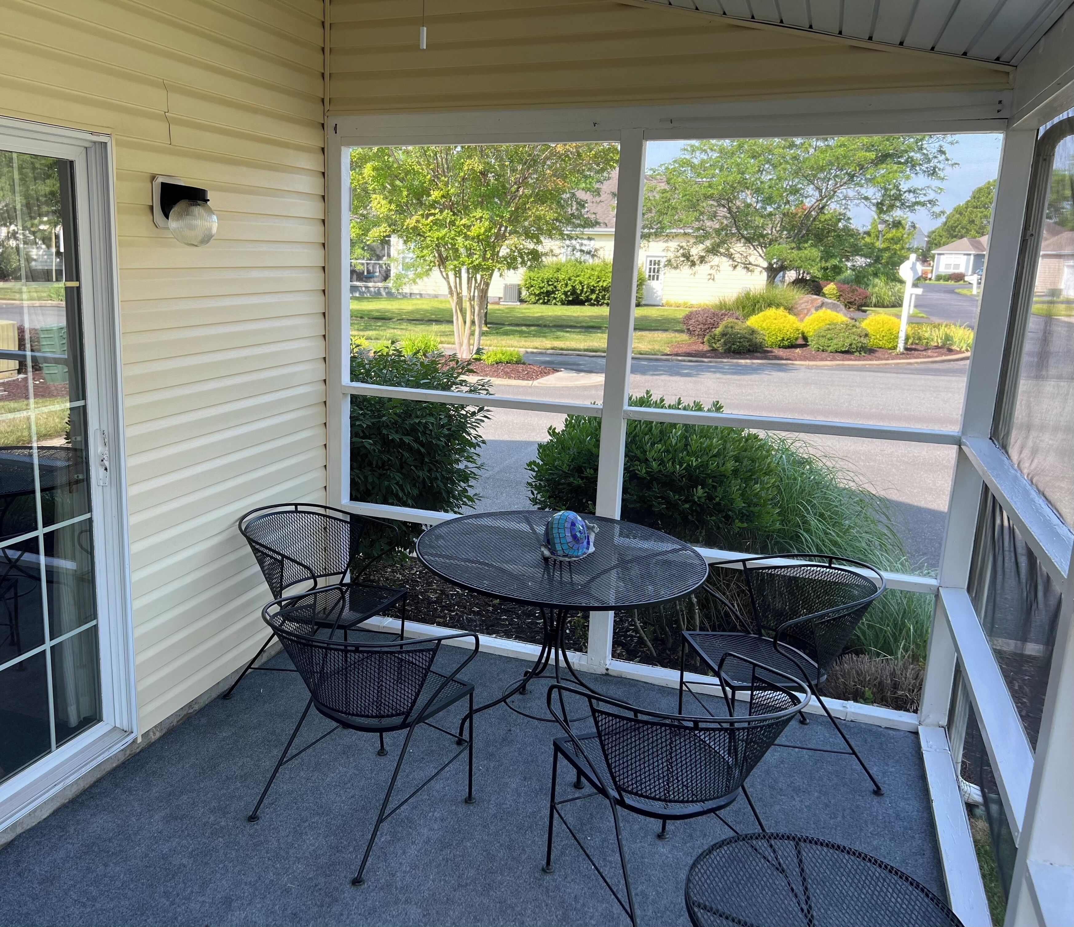 Un patio cubierto con una mesa y sillas, vista a una calle residencial y una casa al fondo.