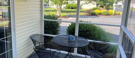 Un patio cubierto con una mesa y sillas, vista a una calle residencial y una casa al fondo.