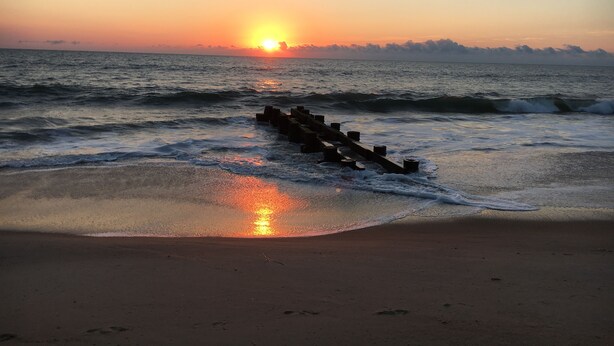 Un atardecer sobre el océano con una estructura de madera en el agua.