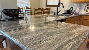 Una cocina con encimera de granito, sillas de madera y una ventana con persianas.