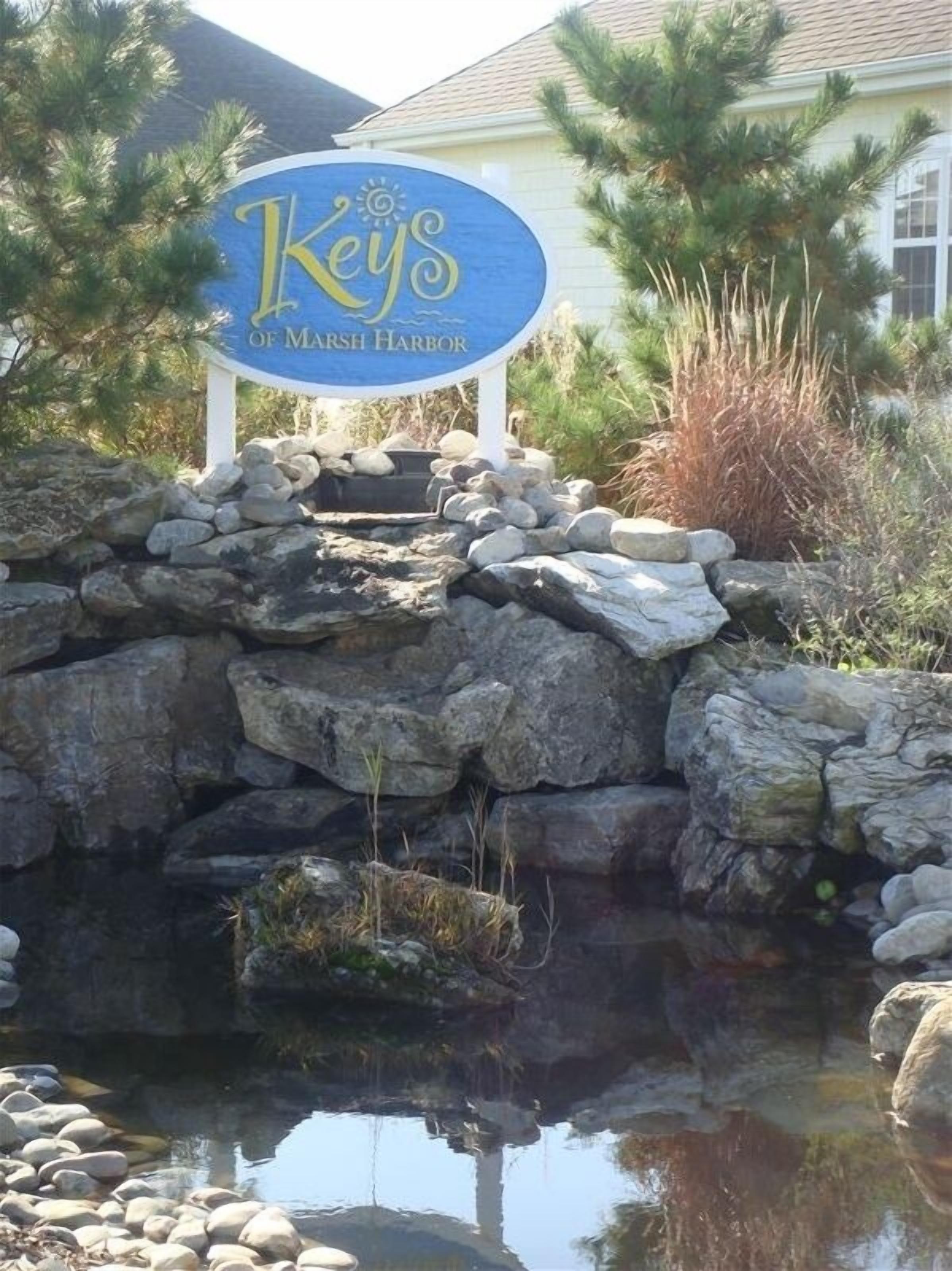 A sign for 'Keys of Marsh Harbor' with a stone wall and a small pond in front.