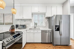 Una cocina moderna con armarios blancos, un refrigerador de acero inoxidable, lavavajillas integrado, estufa a gas y una ventana con persianas.