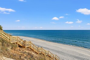 A beach with wooden stairs leading down to the shore, a clear blue sky, and calm ocean waves.
