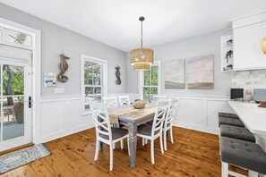 A dining area with a wooden table, white chairs, a woven pendant light, and artwork on the walls. - Relaxing pet-friendly cottage — 4 bikes to explore 30A & just steps to the pool (Seacrest Beach West)