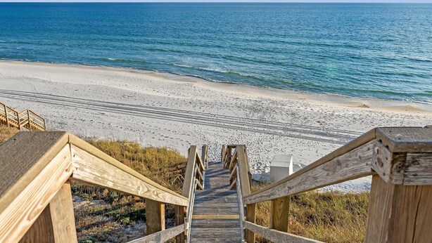 Una escalera de madera que lleva a una playa con vistas despejadas al océano.