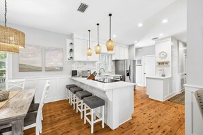 Une cuisine moderne avec des meubles blancs, un îlot central doté de tabourets de bar, un éclairage suspendu et un plancher en bois.