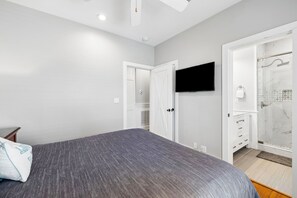 Une chambre à coucher avec un lit, un téléviseur fixé au mur et un dressing avec douche.