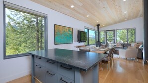 Une cuisine moderne dotée d’un grand îlot central, d’un plafond en bois et de grandes fenêtres offrant une vue sur les arbres.