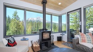 Un salon moderne doté d’une grande cheminée, d’un canapé, d’une table basse et offrant une vue sur un paysage montagneux grâce à de grandes fenêtres.