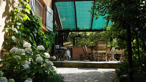 Un espace extérieur aménagé en terrasse, avec une table et des chaises, entouré d’une végétation luxuriante et de fleurs blanches.
