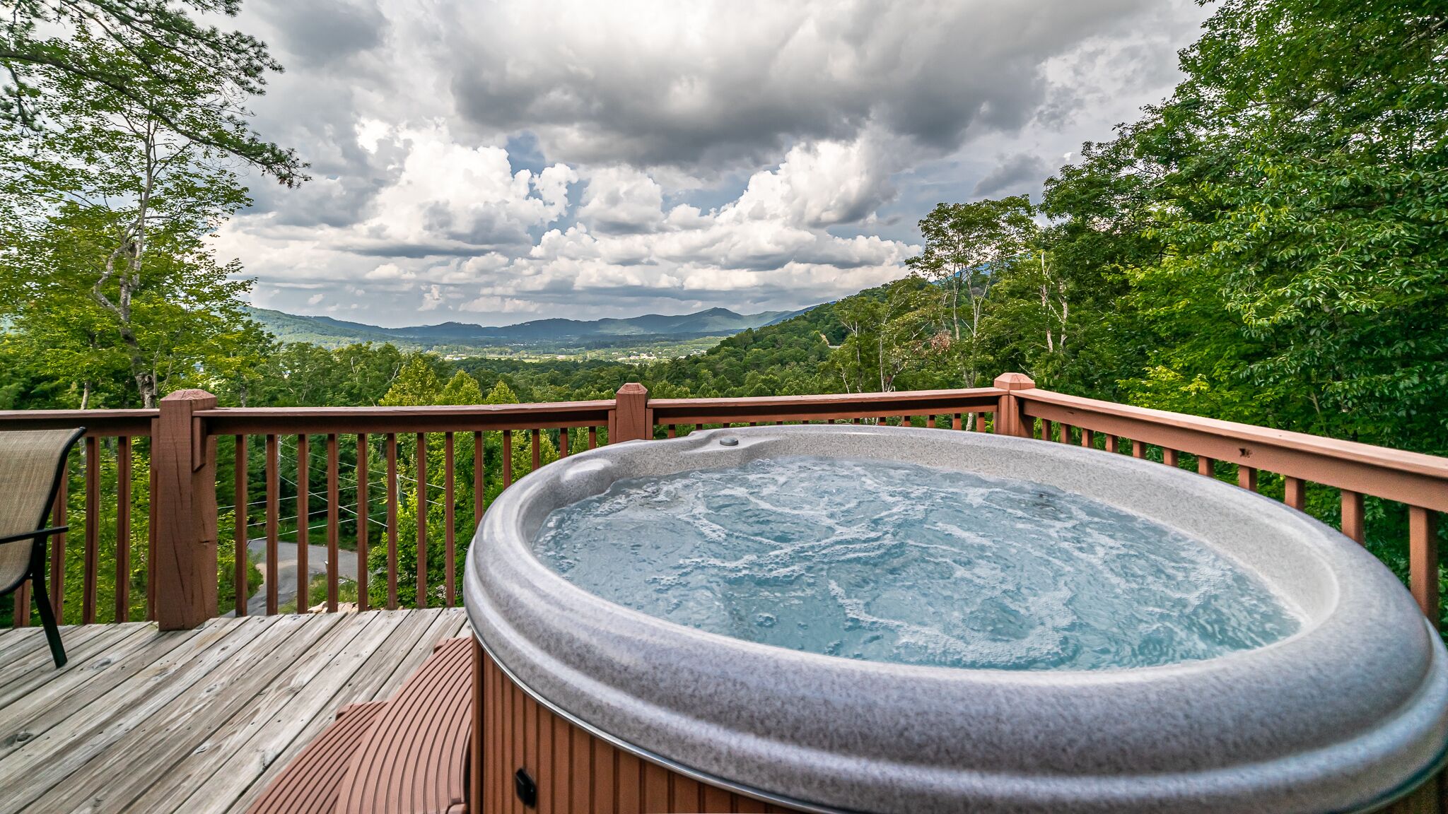 Een hottub op een houten terras met uitzicht op bergen en bomen.