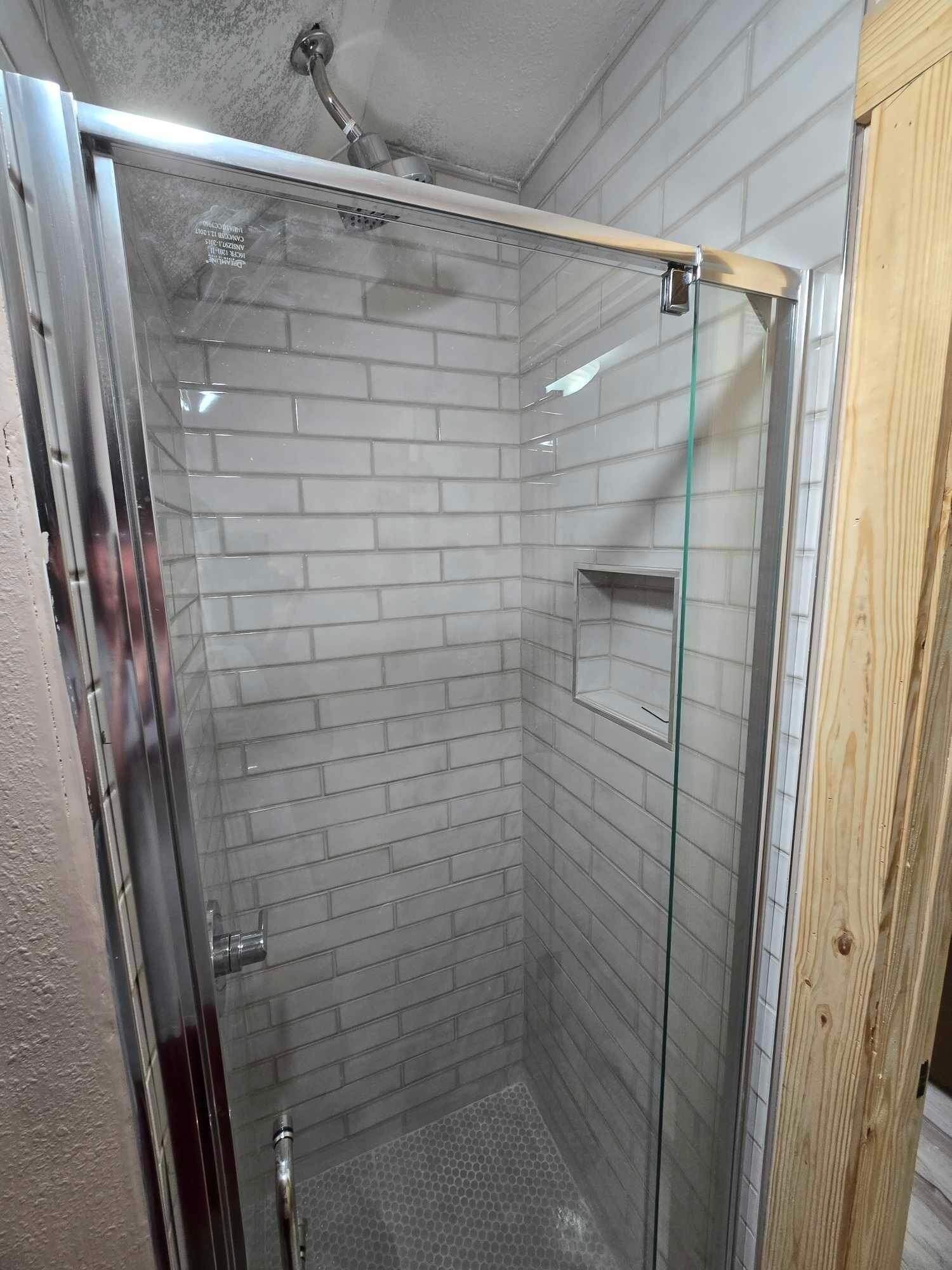 A shower with glass doors, white tiled walls, and a wooden door frame.