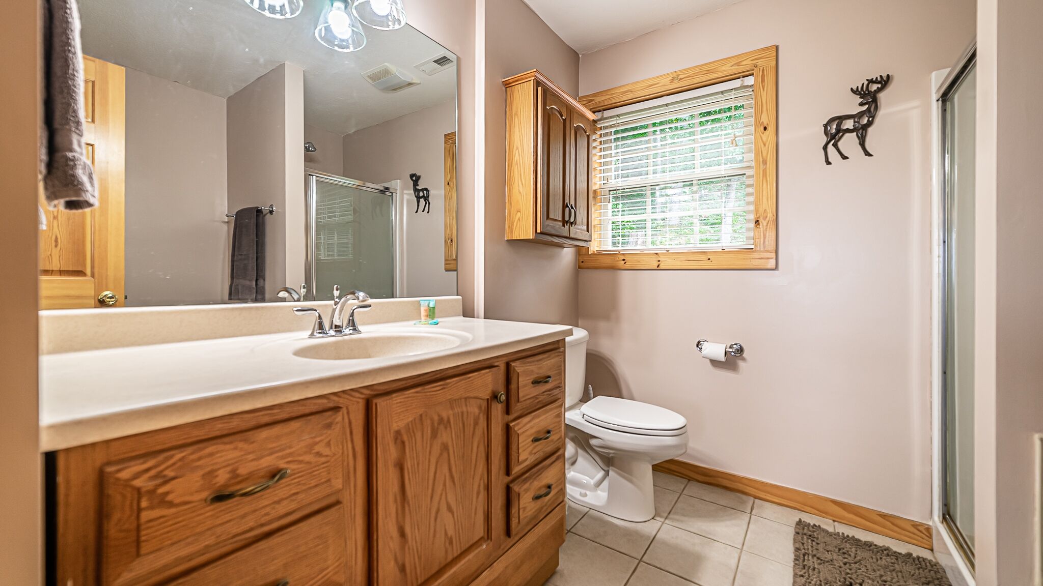 A bathroom with wooden cabinets, a white sink, a toilet, and a window with blinds.