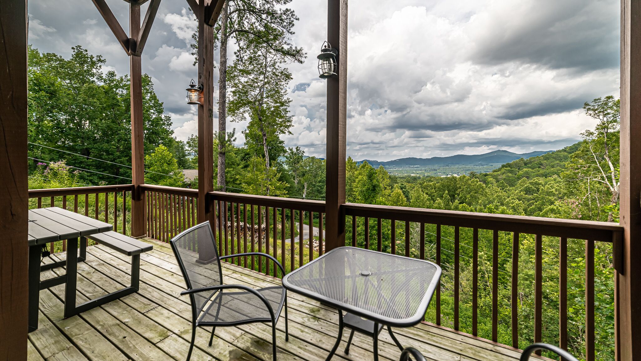 A wooden deck with two tables and chairs, overlooking a lush landscape with mountains in the distance.