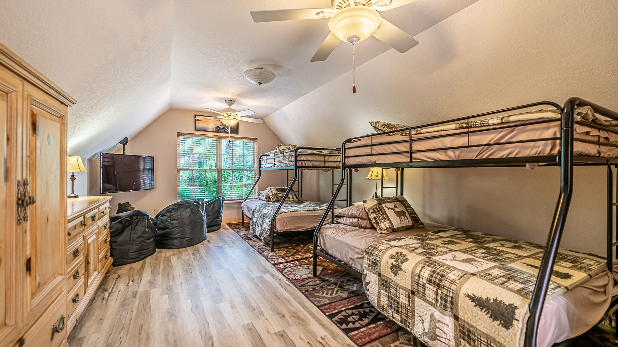 Ein Schlafsaalzimmer mit Etagenbetten, Deckenventilator, Fernseher und einem Fenster mit Jalousien.