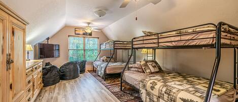 Ein Schlafsaalzimmer mit Etagenbetten, Deckenventilator, Fernseher und einem Fenster mit Jalousien.