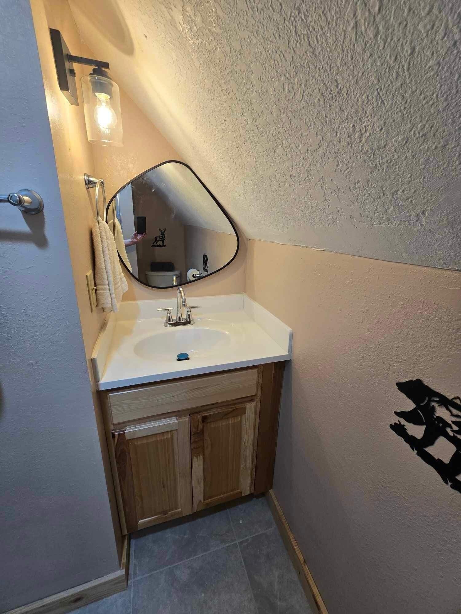 A bathroom with a white sink, wooden cabinets, a mirror, and a towel rack.