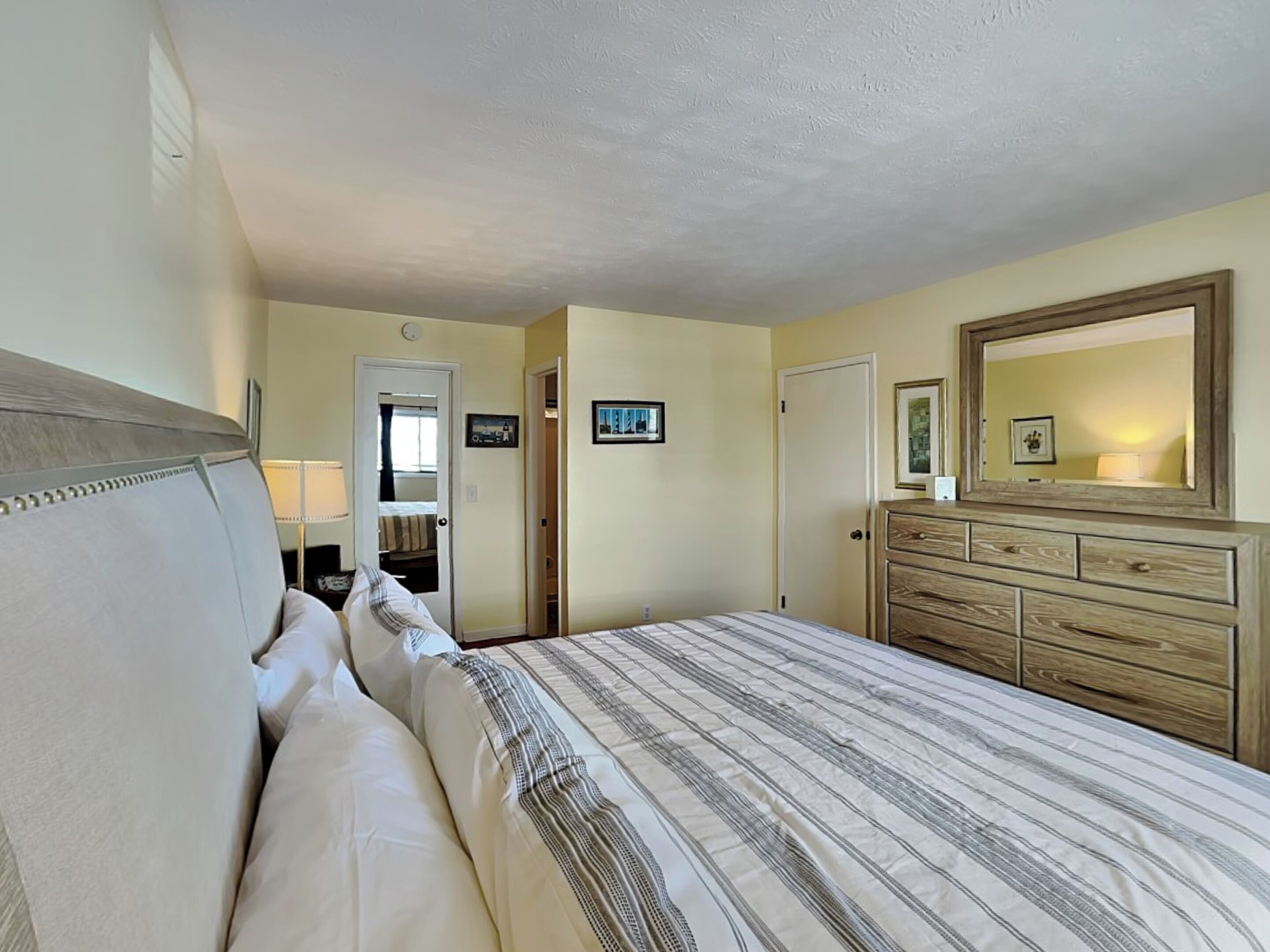 Une chambre à coucher comprenant un lit, une commode, un miroir et une porte donnant sur une salle de bain.