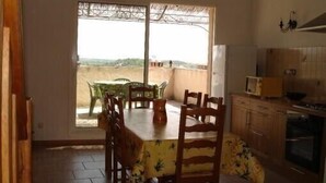 A dining area with a table and chairs, a kitchen with cabinets and appliances, and a view through a window. - Close to the Gorges du Verdon Apartment with garden, terrace, panoramic view (Puimoisson)