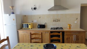 A kitchen with a refrigerator, microwave, stove, and a table with a bowl. - Close to the Gorges du Verdon Apartment with garden, terrace, panoramic view (Puimoisson)