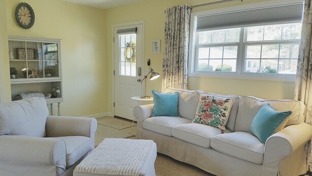 A living room with a beige sofa, two armchairs, a small table, and a lamp. There is a window with curtains and a door with a wreath. - We welcome Short & Long Term Guest .  (Aiken)