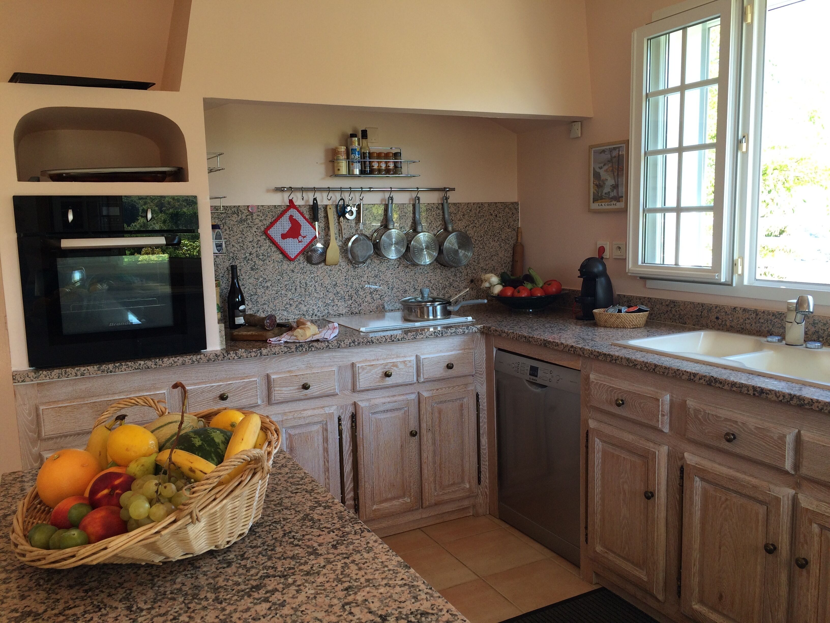 A kitchen with granite countertops, wooden cabinets, a built-in oven, a dishwasher, and a window with a view of greenery.