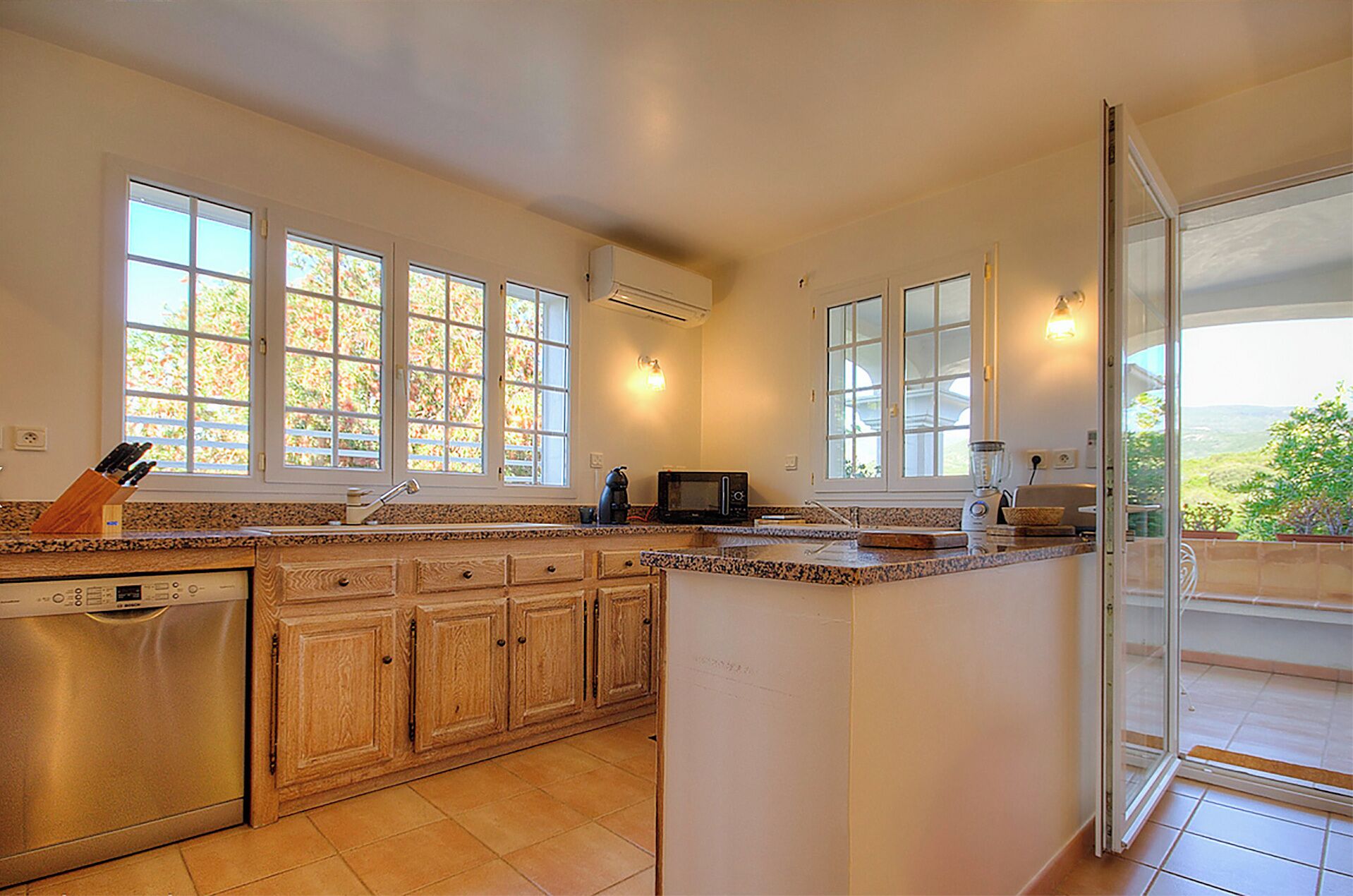 Una cocina amplia con ventanas grandes, lavavajillas, armarios de madera y horno integrado.