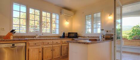 Una cocina amplia con ventanas grandes, lavavajillas, armarios de madera y horno integrado.