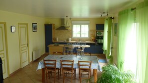 Een eetgedeelte met een tafel en stoelen, een keuken achtergrond en een raam met gordijnen.